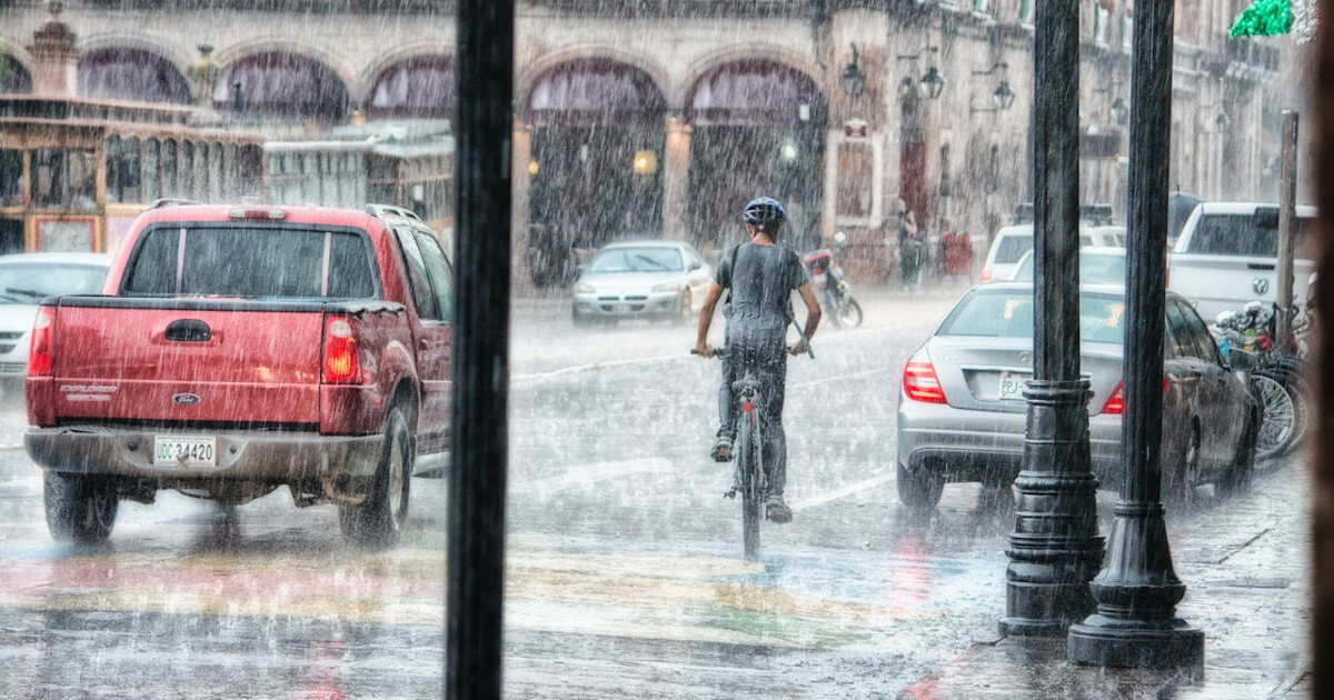 8 Ways to Sell More Flood Insurance - person on bike and lots of cars on the road with heavy rain by pexels-genaro-servín-763398